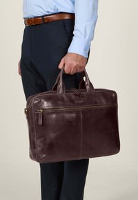 Brun lærveske med doble håndtak, glidelåslukking og frontlomme. Glatt tekstur, rektangulær form, egnet for profesjonelt bruk.