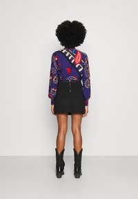 Camisa de manga larga con un patrón de paisley colorido en azul, rojo y amarillo, combinada con una minifalda negra con un cinturón con tachuelas. Botas negras.