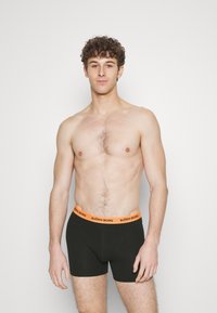 Čierne boxerky s oranžovým pásom s logom "BJÖRN BORG", vyrobené z elastického materiálu, s priliehavým strihom.