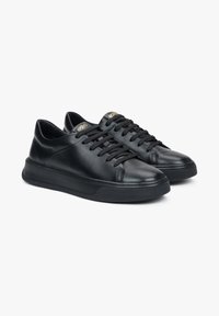 Czarne skórzane sneakersy z okrągłym noskiem, płaskimi czarnymi sznurowadłami i teksturowaną czarną gumową podeszwą. Zawierają złote logo na języku.