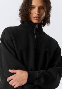 Felpa nera con collo alto e mezza cerniera. Caratterizzata da vestibilità comoda e tessuto morbido e liscio con maniche con polsini.