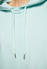 Felpa blu chiaro con una texture morbida. Presenta coulisse con punte metalliche e una vestibilità rilassata. Il tessuto è liscio e senza motivo.