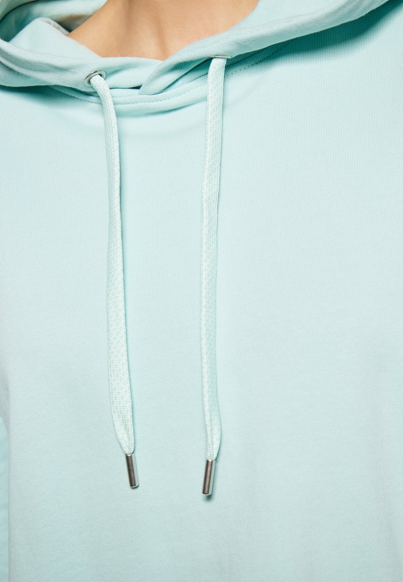Felpa blu chiaro con una texture morbida. Presenta coulisse con punte metalliche e una vestibilità rilassata. Il tessuto è liscio e senza motivo.