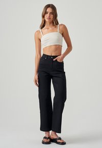 Črne visoke hlače z ravnim krojem, v kombinaciji s kremno kratko majico. Model nosi črne ravne sandale.