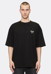 Tricou negru supradimensionat din bumbac, cu guler rotund și mâneci scurte, având un logo alb mic imprimat pe pieptul stâng.