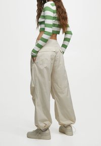 Grünes und weiß gestreiftes Croptop kombiniert mit beigen Cargo-Hosen mit gerafften Bündchen und Seitentaschen. Die Schuhe sind beigen Plateausneaker.