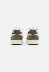 Sneaker bianche con dettagli in suede verde, pannello di pelle marrone sul tallone e suola in gomma chiara. Presenta una piccola grafica di un albero sul tallone.