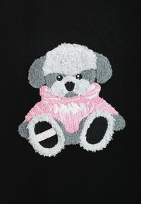 Oso de peluche bordado con suéter rosa sobre un fondo de tela negra. El oso tiene pelaje gris y blanco, con rasgos faciales detallados.