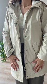 Beige vízálló dzseki cipzárral az elején, patentos záródású és oldalsó zsebekkel. Puha béléssel és állítható kapucnival rendelkezik.