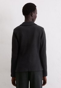 Black pinstriped blazer made of textured fabric with a notched collar, tailored fit, and long sleeves, viewed from the back.