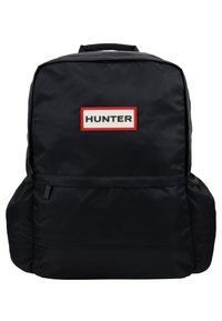 Sac à dos noir avec poches latérales et poche avant zippée, avec une étiquette rectangulaire blanche et rouge avec le mot "HUNTER" au centre.