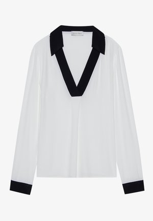 Haut à manches longues blanc avec un col en V noir et des poignets noirs. Tissu lisse avec une coupe décontractée et un design minimal.