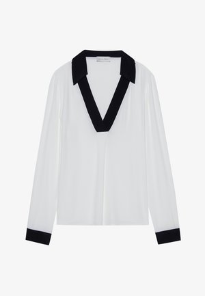Haut à manches longues blanc avec un col en V noir et des poignets noirs. Tissu lisse avec une coupe décontractée et un design minimal.