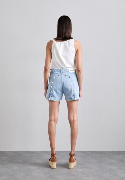Shorts en denim bleu clair avec des accents de boutons sur les côtés, ourlet brut, et un débardeur blanc. Des escarpins en espadrille marron complètent la tenue.