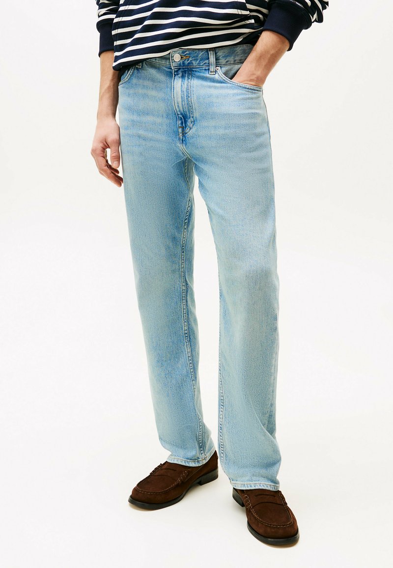 Jeans in denim blu chiaro con taglio dritto, dotati di cinque tasche e finitura strutturata. Indossati con mocassini marrone scuro.