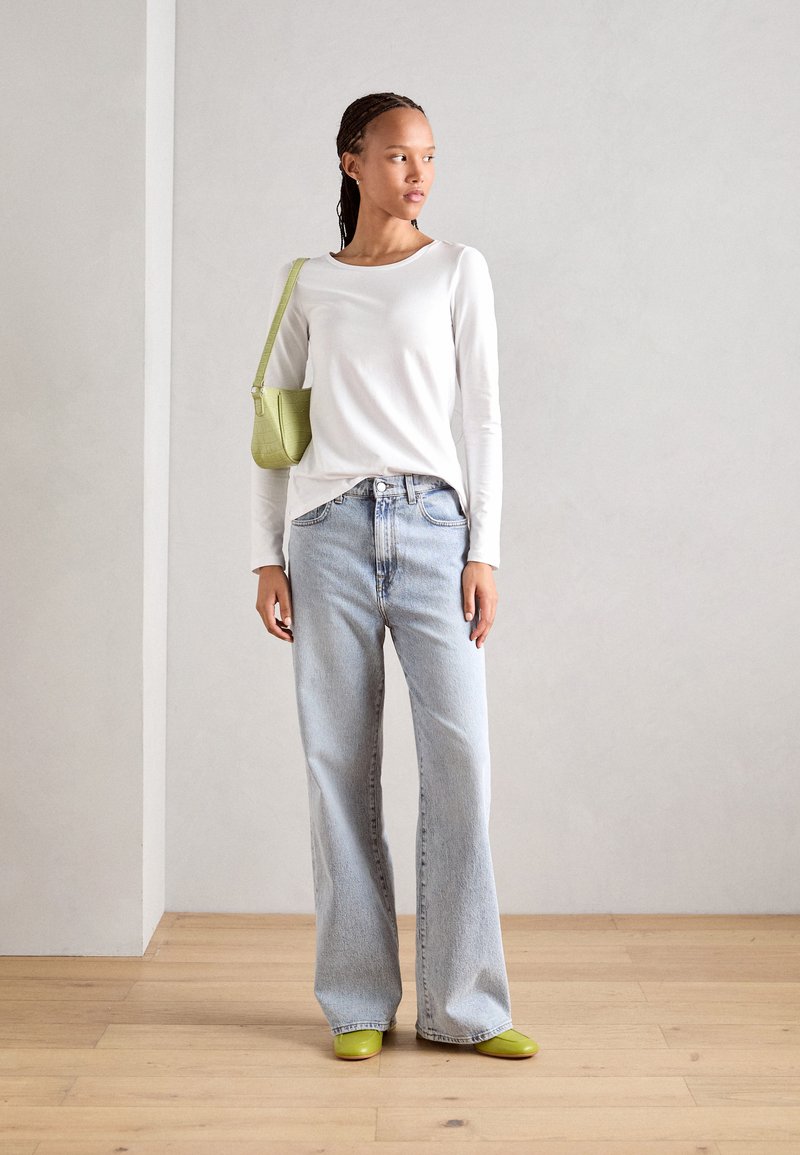 White long-sleeve top, light blue wide-leg jeans, green handbag, and bright green shoes. Smooth fabric and relaxed fit.