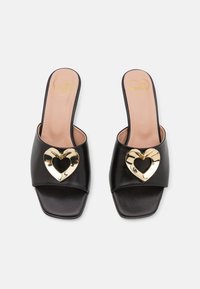 Black slide sandals made of leather featuring a center gold heart detail. Open-toe design with flat soles and smooth textured finish.
