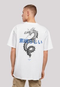 White oversized t-shirt featuring a large black dragon graphic on the back and blue text. Short sleeves and a relaxed fit.