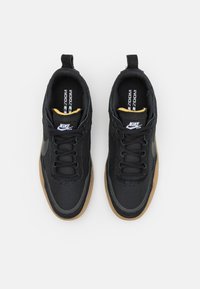 Black Nike sneakers with a textured upper, a gum sole, and a yellow accent on the tongue. Features black laces and side logo.