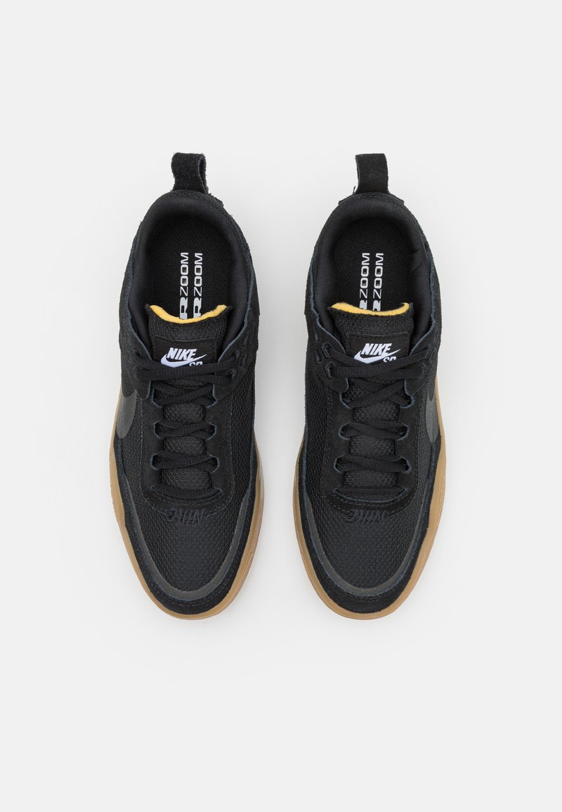 Baskets Nike noires avec une tige texturée, une semelle en caoutchouc et un accent jaune sur la languette. Dotées de lacets noirs et d'un logo sur le côté.