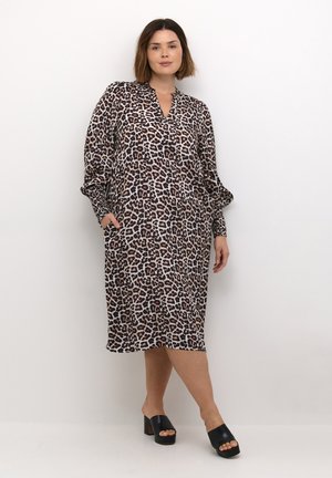 Kleid mit Leopardenmuster, langen Ärmeln, V-Ausschnitt, fließendem Stoff, zwei Seitentaschen und Länge bis zur Mitte der Wade. Getragen mit schwarzen Blockabsatzsandalen.
