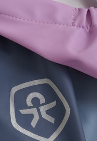 Färggart vattentålig tyg med ett rosa överlager och en mörkblå botten, med en silverlogotyp och synliga sömdetaljer.