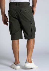 Shorts cargo en coton vert foncé, avec deux poches latérales et deux poches arrière avec des fermetures à bouton. L'ourlet tombe juste au-dessus du genou.