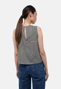 Top sans manches en noir et blanc avec des motifs de rayures géométriques. Dispose d'un détail en trou de serrure à l'arrière. Fabriqué en tissu léger.