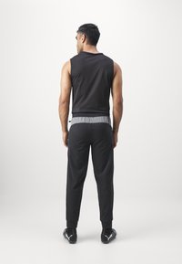 Zwarte mouwloze top gecombineerd met grijze broek met tailleband. De broek heeft een taps toelopende pasvorm en elastische boorden. Zwarte sportieve schoenen met logo-detail.