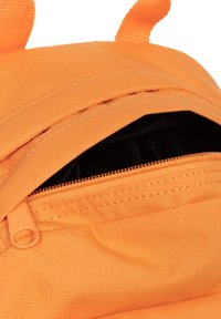 Oranžový batoh s kapsou na zip. Vnější strana má texturovanou tkaninu a zesílené švy. Vnitřek je podšitý černou tkaninou.