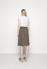 Falda verde oliva, hasta la rodilla, con cintura elástica. Combinada con una camiseta blanca y sandalias de plataforma. Textura suave, diseño simple.