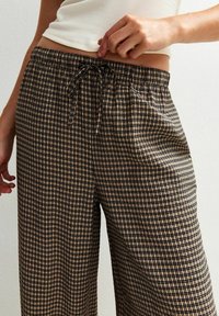 Pair of wide-leg pants in a beige and black grid pattern, featuring a drawstring waist and soft, textured fabric.