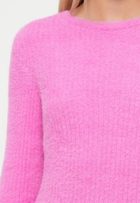 Futrzasty różowy sweter o prążkowanej fakturze, z okrągłym dekoltem i długimi rękawami, podkreślający miękkość i ciepło.