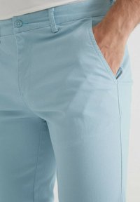 Chinos en coton bleu clair avec une texture lisse, coupe slim, deux poches avant et une discrète fermeture à bouton à la taille.