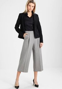 Blazer nero sopra una camicia nera con bottoni, abbinata a pantaloni grigi a gamba larga a vita alta. Completa l'outfit un paio di décolleté nere con punta affilata.