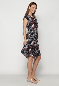 Rochie florală cu un fundal negru și modele de frunze roșii, albastre și albe; design fără mâneci; talie legată; hem asimetric.