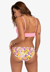 Růžový bikini top s nastavitelnými ramínky v kombinaci s bikini kalhotkami s květinovým vzorem v žluté, růžové a černé barvě. Měkká tkanina s detailem na zavazování na boku.