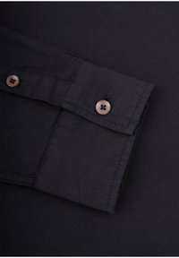 Sort skjorte stof med en foldet manchet og to brune knaplukninger, der viser en glat tekstur og et enkelt design.