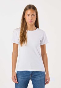 Hvid bomuldst-shirt med rund halsudskæring og korte ærmer, kombineret med blå jeans. Glat tekstur uden synlige mønstre eller detaljer.