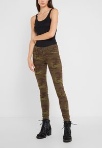 Kamouflagejeans i bruna och gröna nyanser, slim fit med midja i normalhöjd, kombinerat med svarta snörkängor.