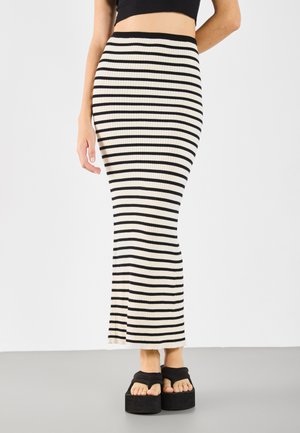 Jupe maxi en tricot à rayures verticales noires et crème, présentant un design ajusté. Associée à des sandales compensées noires imposantes.