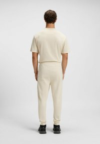 Beiges Kurzarmoberteil und passende Hose aus weichem Material, mit elastischem Bund und konischer Beinform, kombiniert mit schwarzen Schuhen.