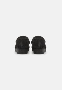 Svarte fløyelslipper med myk tekstur, rund bak, og flate såler. Har et enkelt design uten synlig maskinvare eller aksenter.