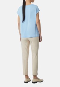 Jasnoniebieska bluzka z krótkim rękawem o luźnym kroju, zestawiona z beżowymi eleganckimi spodniami. Bluzka ma okrągły dekolt; spodnie mają boczne rozcięcia.