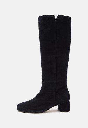 Botte noire en daim jusqu’au genou avec bout arrondi et talon bloc, présentée de côté sur un fond clair et uni.
