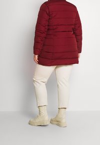 Burgunderfärgad puffjacka med horisontell quiltad design, i kombination med ljusbeiga cropped-byxor och krämfärgade, kraftiga boots.