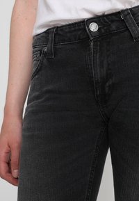 Svarta denimjeans med en klassisk femficksdesign, en framknäppning med knappar och subtila blekningar. Texturen är jämn med en liten stretch.