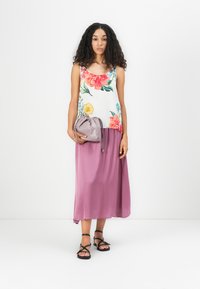 Blomstrete tank topp med levende farger, sammen med et flytende rosa skjørt. Holder en liten grå snorveske. Svart sandaler med stropper.