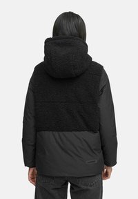 Black jacket featuring a textured fleece back and hood, with smooth fabric on the sleeves and lower part, showcasing a modern design.