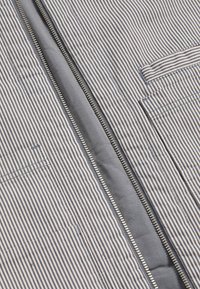 Gestreifte Stoffjacke mit Reißverschluss in Marineblau und Weiß, ausgestattet mit einer Vorderentasche, glattem Material und einem Metallreißverschluss in der Mitte.